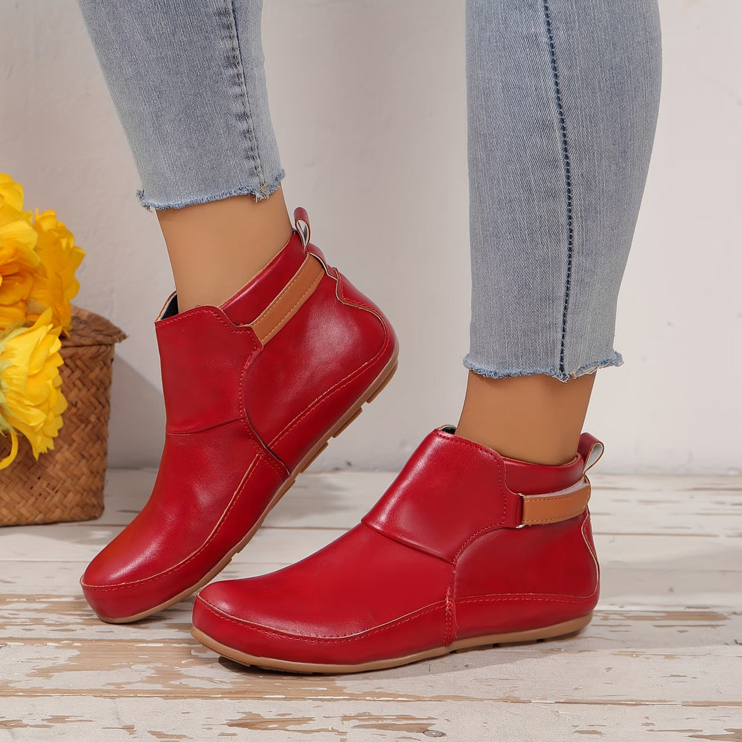 Women's rounded-toe ankle boots with side buckle strap in red, shown with light blue jeans.