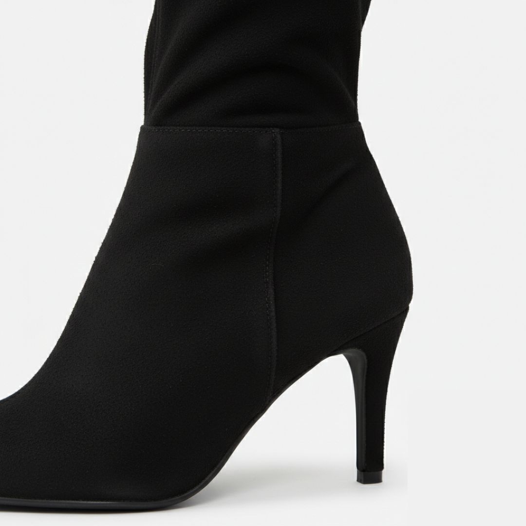 Women's over-the-knee boots with block heel and rounded toe in black suede, paired with a green velvet dress.