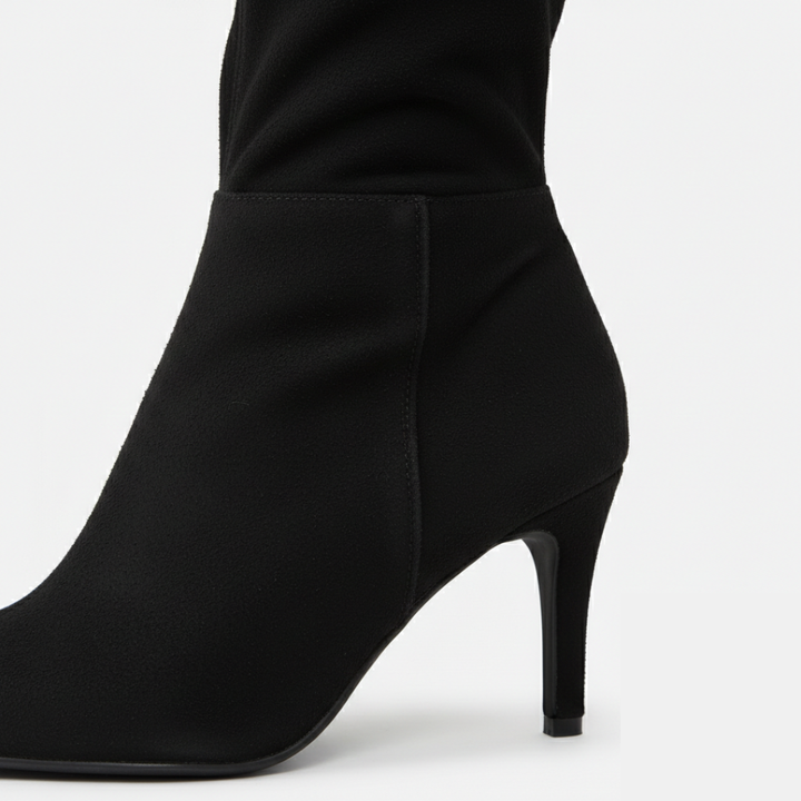 Women's over-the-knee boots with block heel and rounded toe in black suede, paired with a green velvet dress.