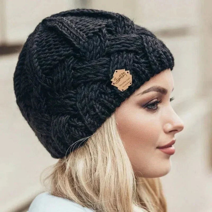 Women's chunky cable knit beanie hat with folded cuff and front badge