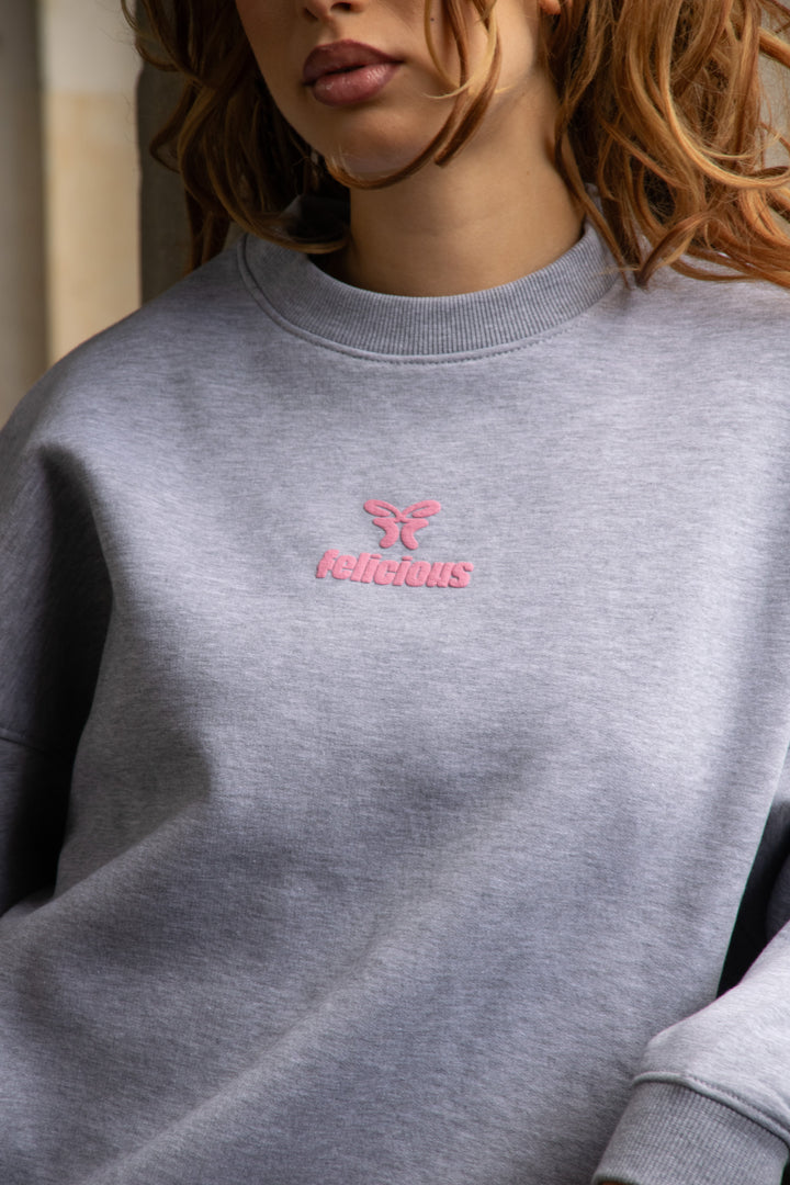 Women's light grey crewneck sweatshirt with pink chest logo and long sleeves