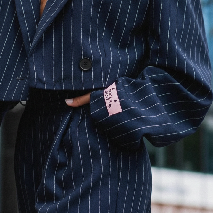 Women's pinstripe trouser suit in navy and grey, shown on two models with white crop top and white trainers.