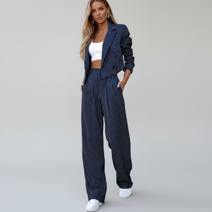 Women's pinstripe trouser suit in navy and grey, shown on two models with white crop top and white trainers.