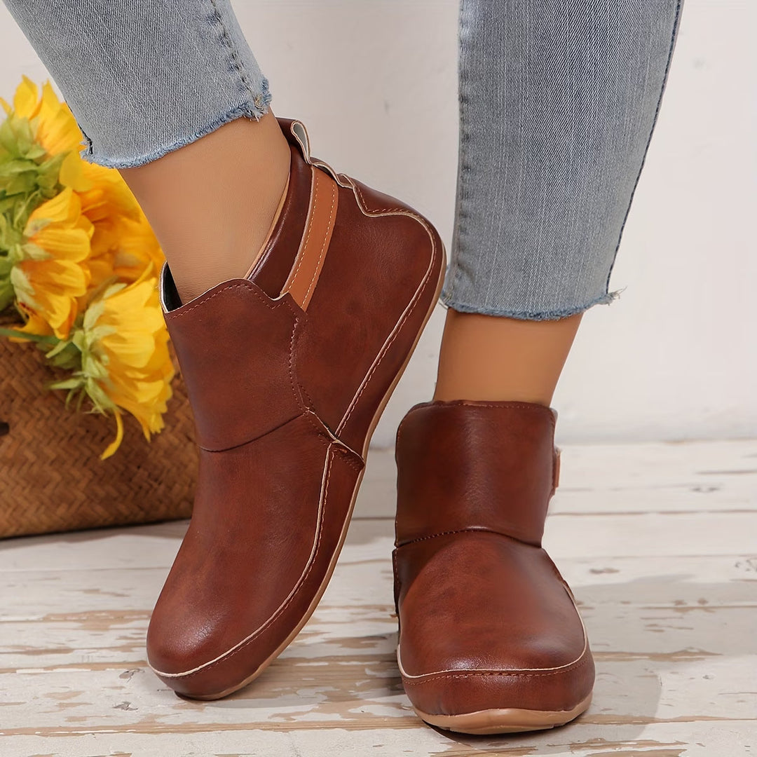 Women's rounded-toe ankle boots with side buckle strap in red, shown with light blue jeans.