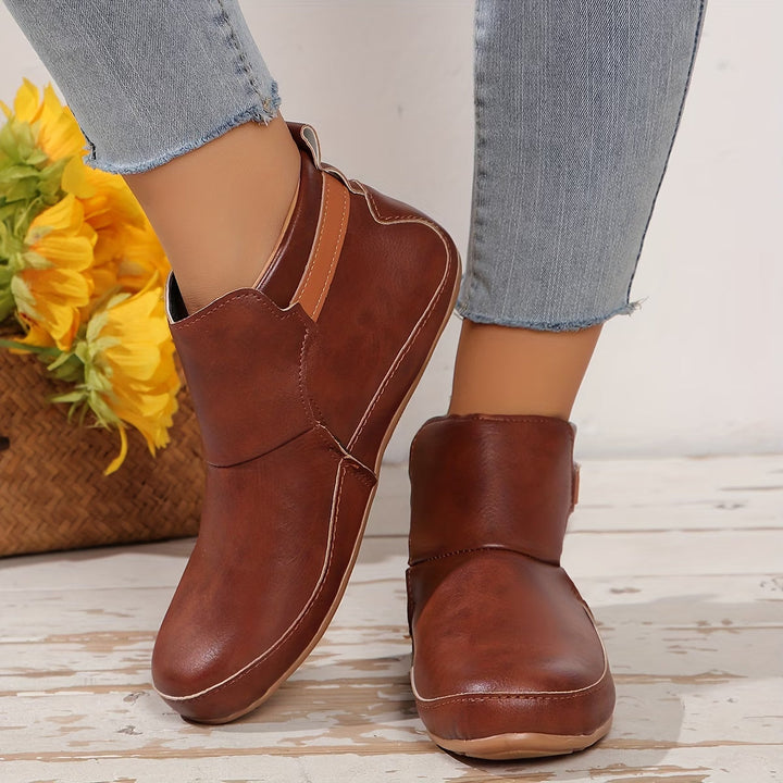 Women's rounded-toe ankle boots with side buckle strap in red, shown with light blue jeans.