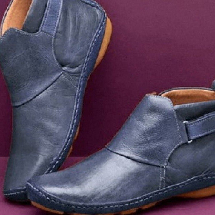 Women's rounded-toe ankle boots with side buckle strap in red, shown with light blue jeans.