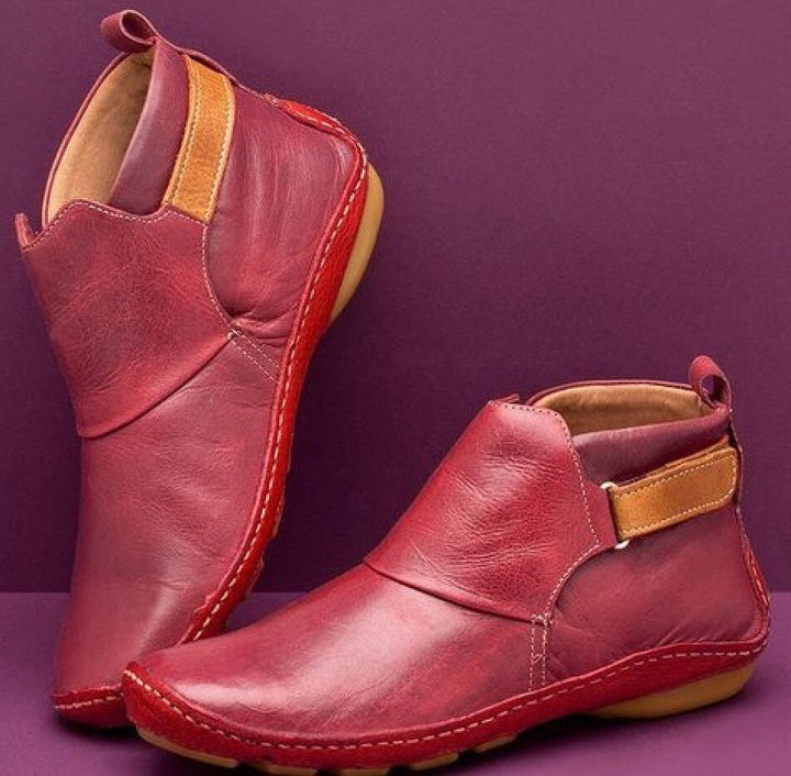 Women's rounded-toe ankle boots with side buckle strap in red, shown with light blue jeans.