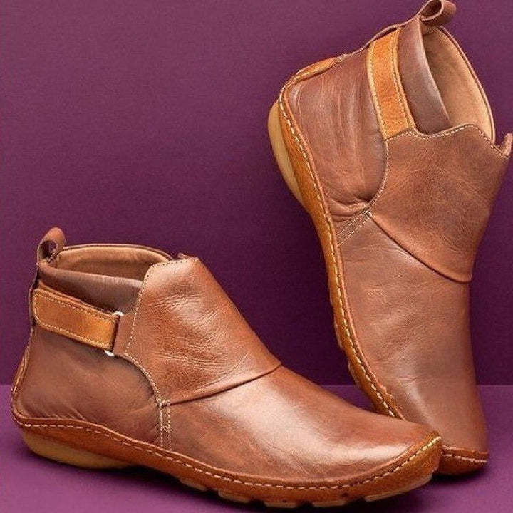 Women's rounded-toe ankle boots with side buckle strap in red, shown with light blue jeans.