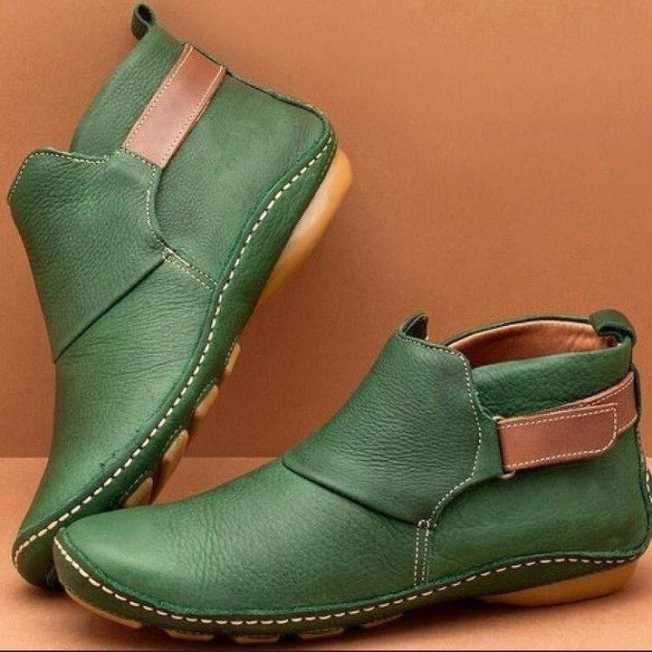 Women's rounded-toe ankle boots with side buckle strap in red, shown with light blue jeans.