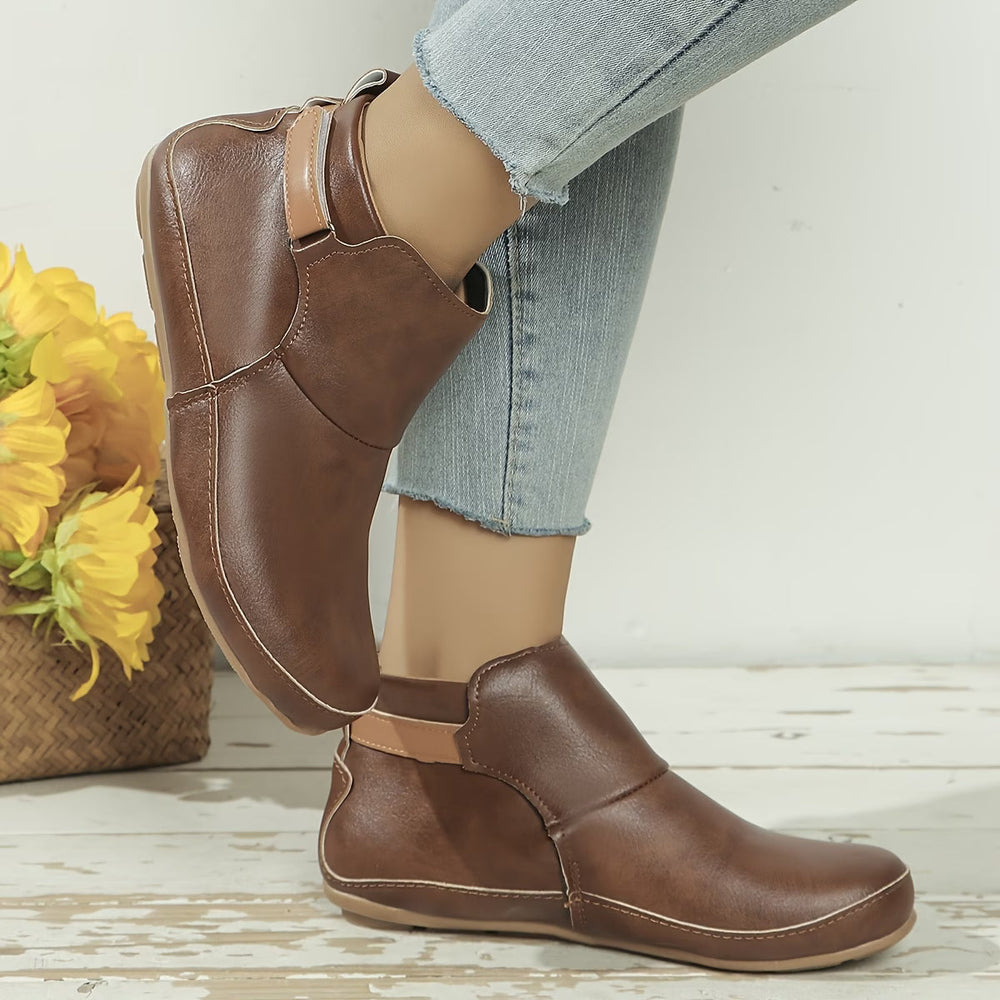 Women's rounded-toe ankle boots with side buckle strap in red, shown with light blue jeans.